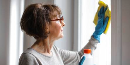 Older woman cleaning a window with a yellow cloth.
